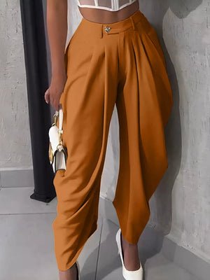 Orange high-waisted pants with sculptural pleats and a button closure.