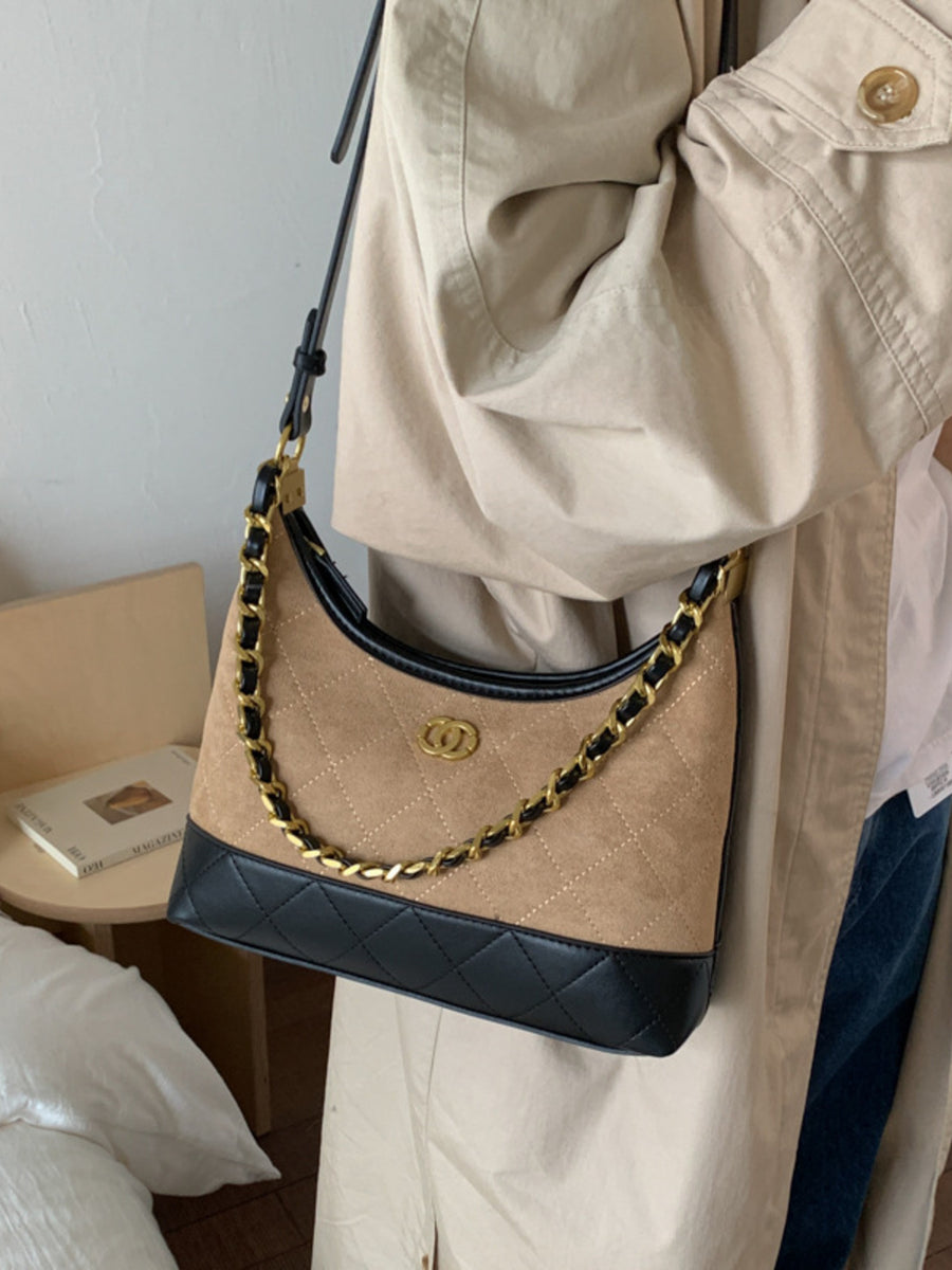 Half-moon crossbody bag in tan suede with black quilted trim and gold chain strap.