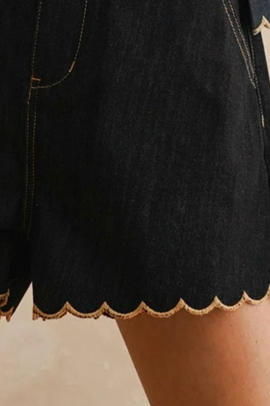 Black denim shorts with scalloped hem and contrast stitching.