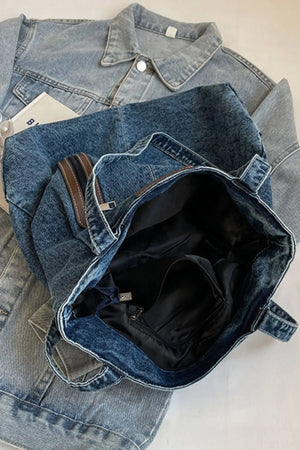 Denim tote bag with leather trim and zippered pocket detail.