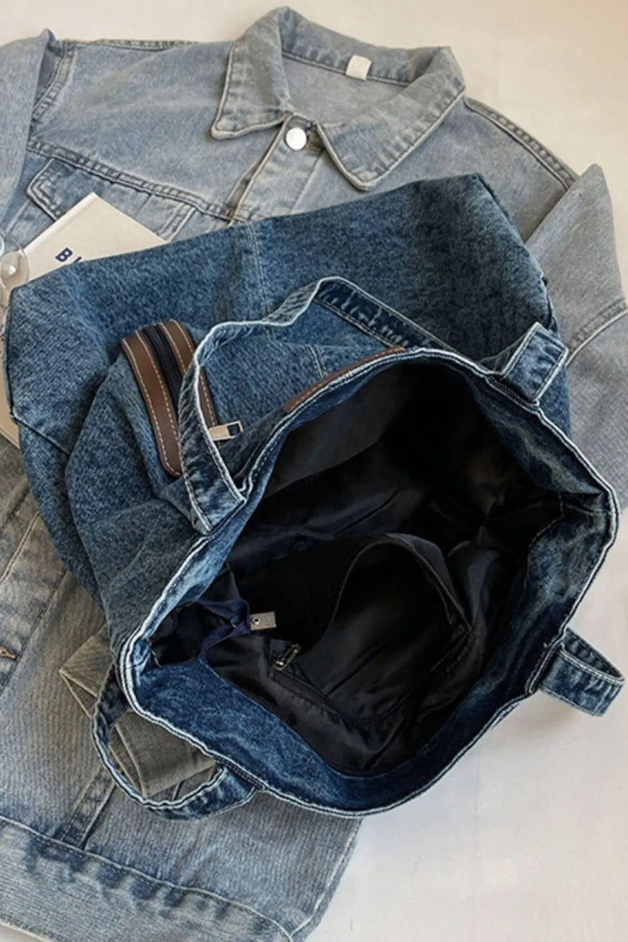 Denim tote bag with leather trim and zippered pocket detail.