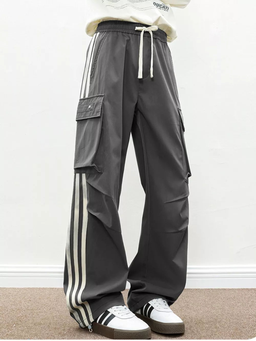 Oversized dark gray cargo pants with white side stripes and flap pockets.