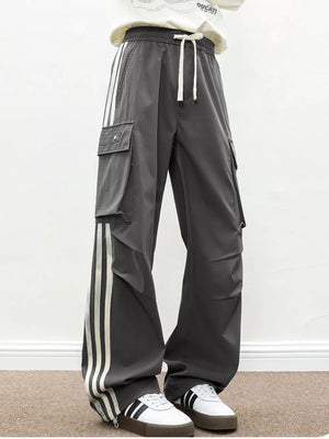 Oversized dark gray cargo pants with white side stripes and flap pockets.