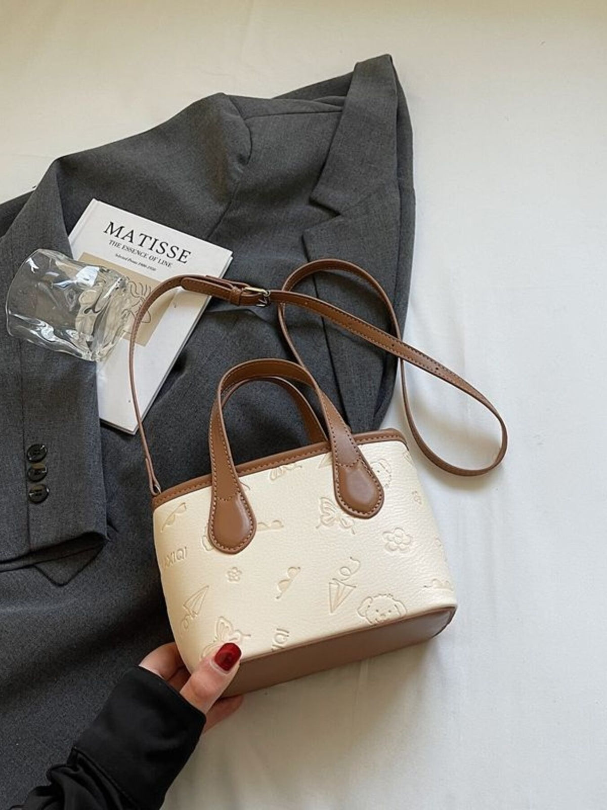 Mini crossbody bag in cream embossed PU leather with brown trim and strap, featuring playful motifs.
