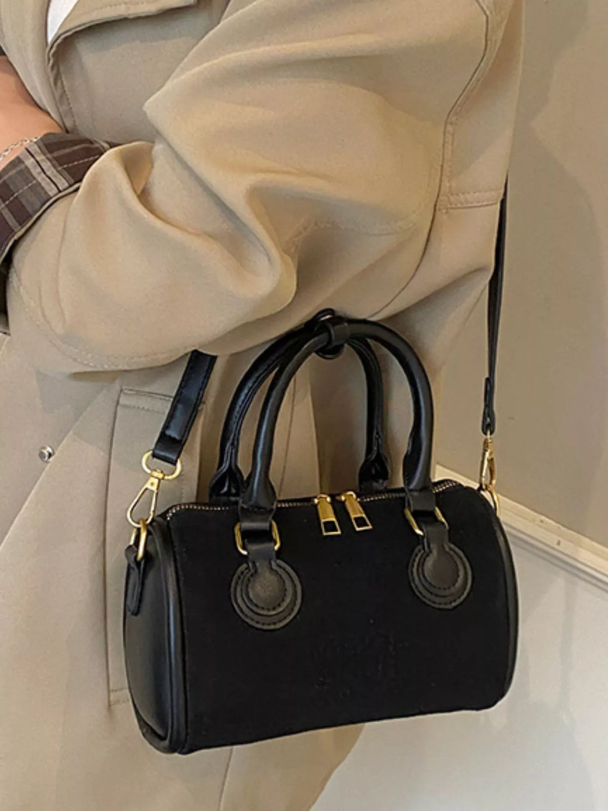 Black barrel crossbody bag with dual top handles and gold hardware.