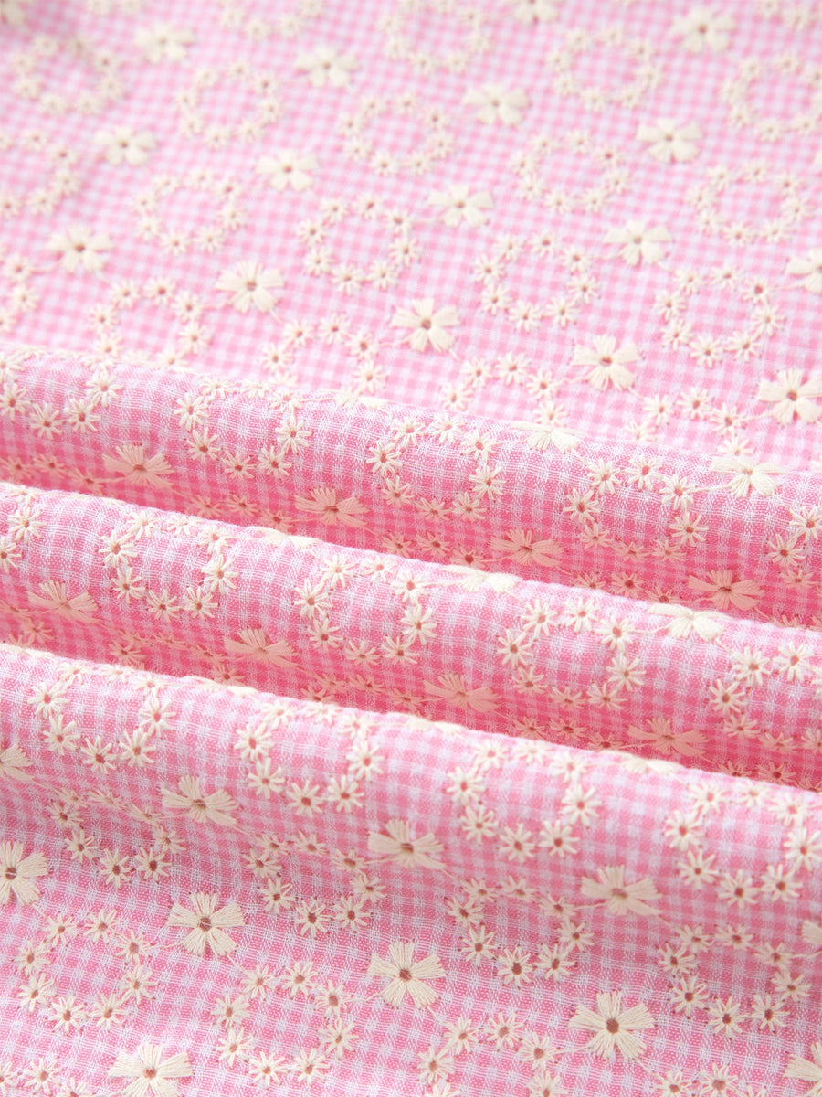 Pink gingham cotton blouse with eyelet floral embroidery and flutter sleeves.