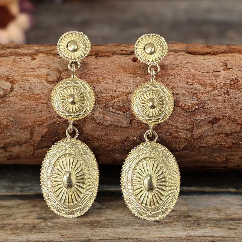 Gold sunburst drop earrings with oval and circular embossed details.