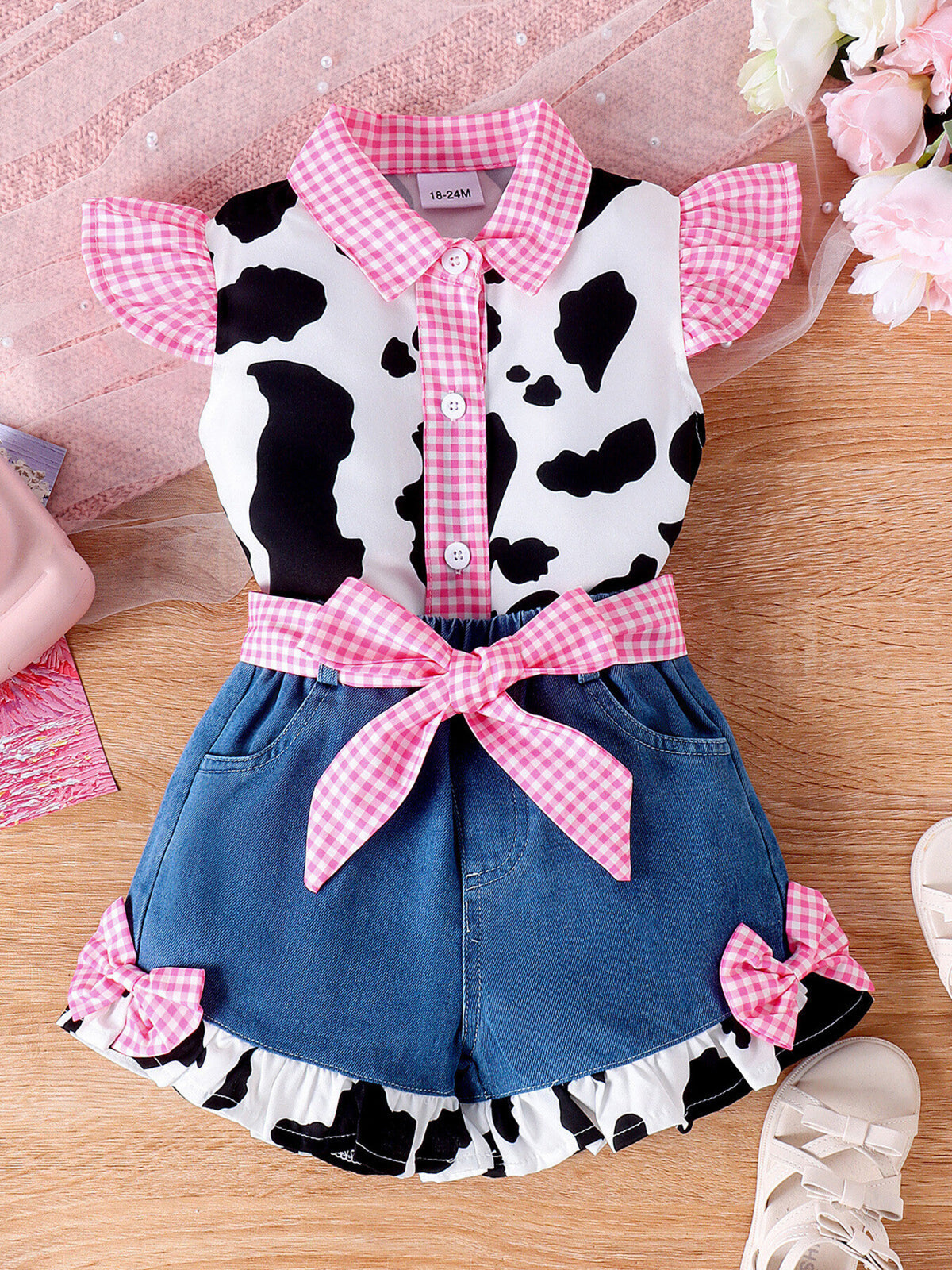 Baby girl cow print top and denim shorts set with pink gingham trim and bow details.
