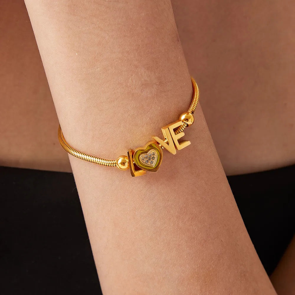 Gold love letter charm bracelet with heart detail and adjustable chain.