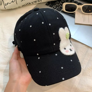 Black polka dot baseball cap with a white bunny applique and green accent.