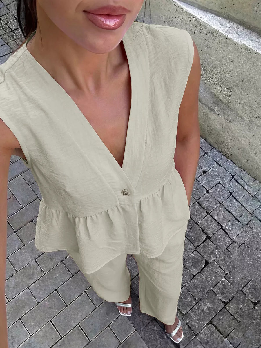 Cream linen blend sleeveless peplum top with V-neck and button detail, paired with wide-leg pants.