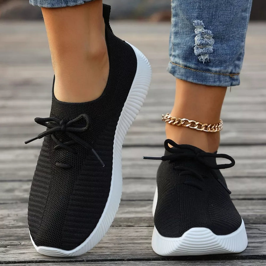Black lace-up sneakers with white mid sole and ribbed knit upper.