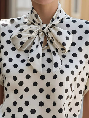 White polka dot shirt with a large black bow tie neck and cap sleeves.