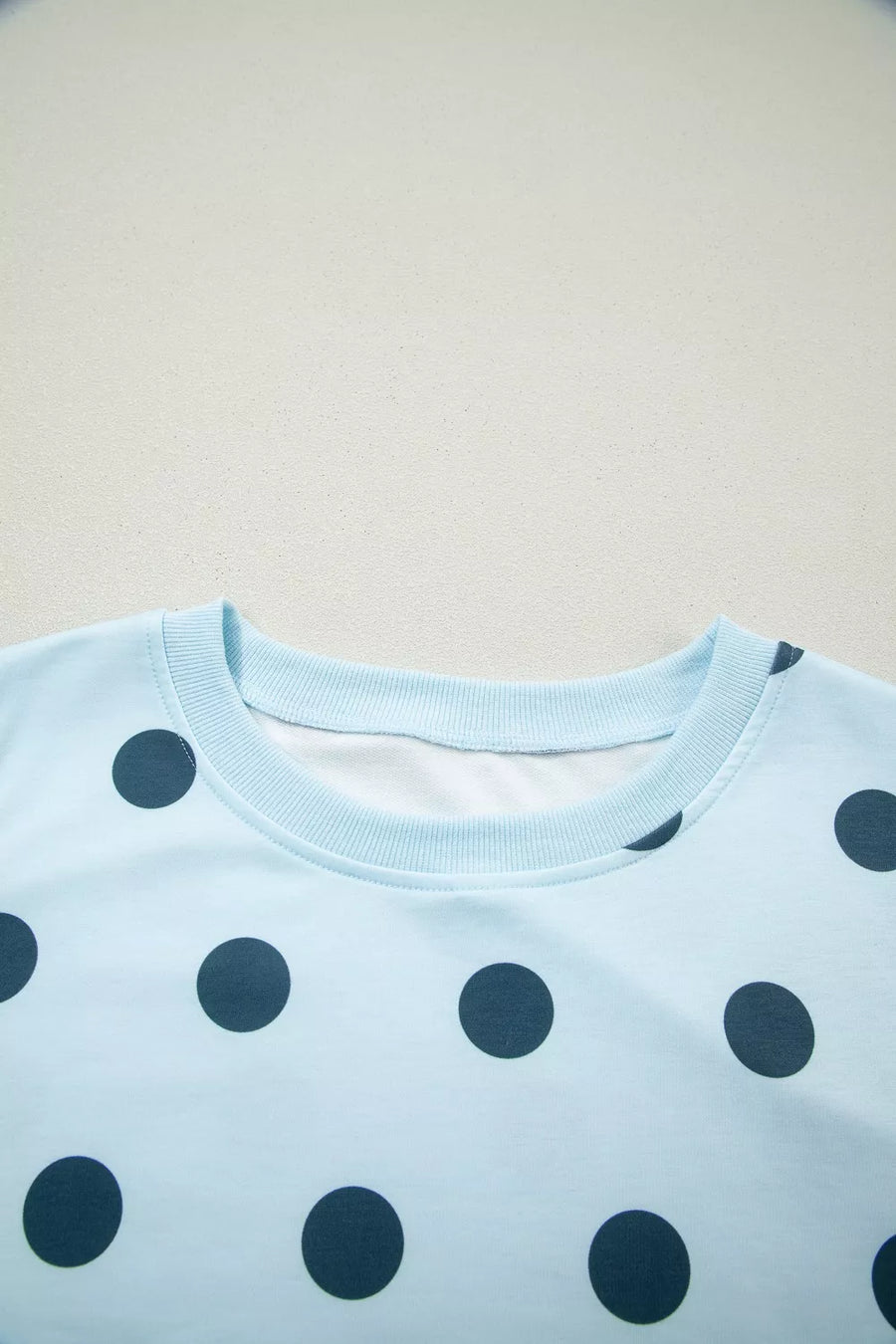 Pastel blue polka dot crew neck top with ribbed collar and cuffs.
