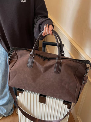 Chocolate duffel bag with leather handles and adjustable strap on a white suitcase.