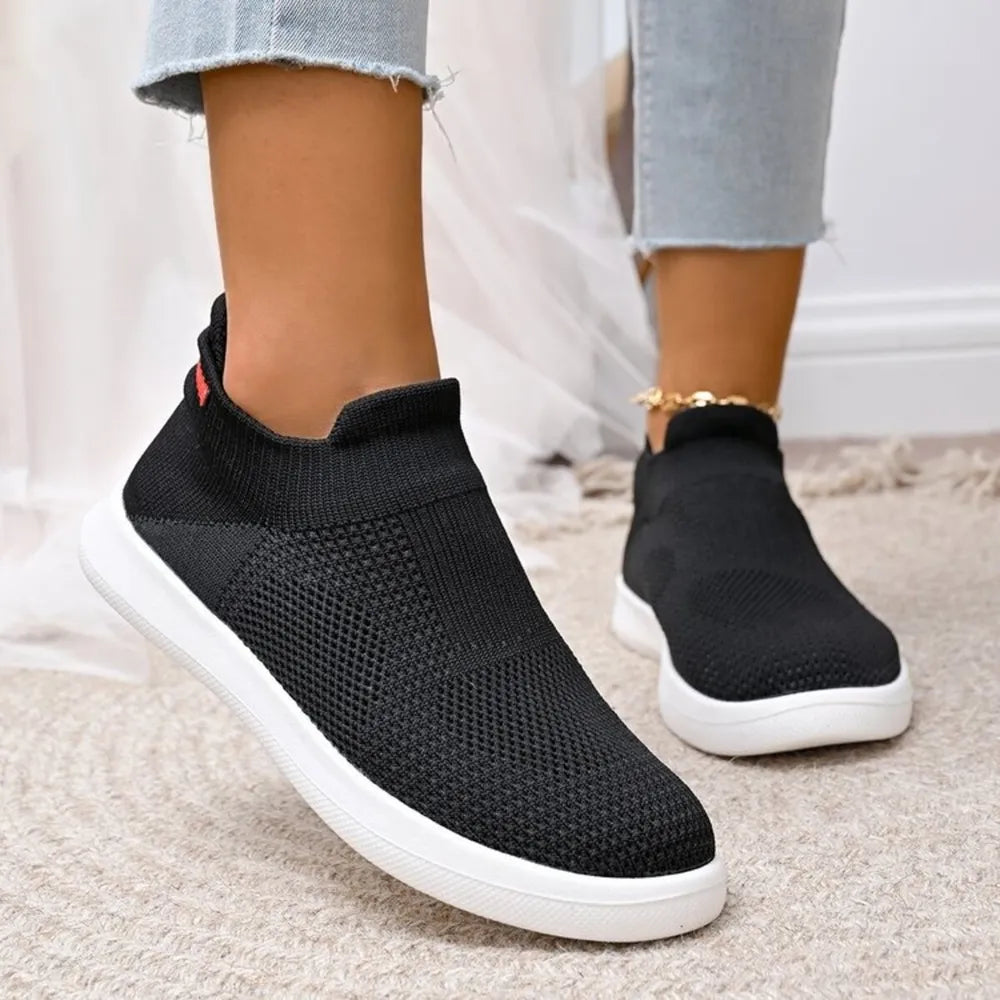 Black knit slip-on sneakers with white soles and a red tab detail.