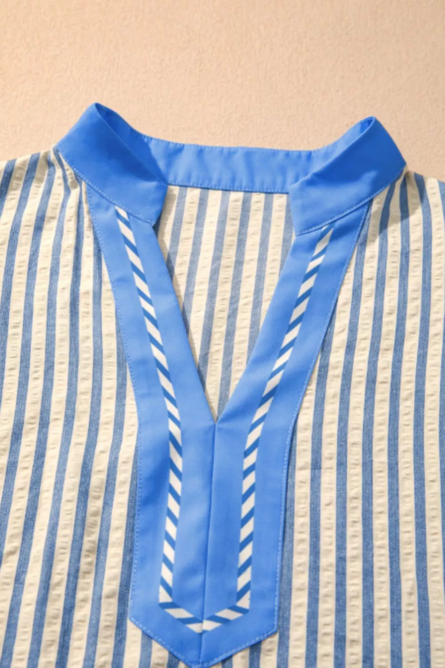Vibrant stripe V-neck shirt with blue color block detail and decorative stitching.