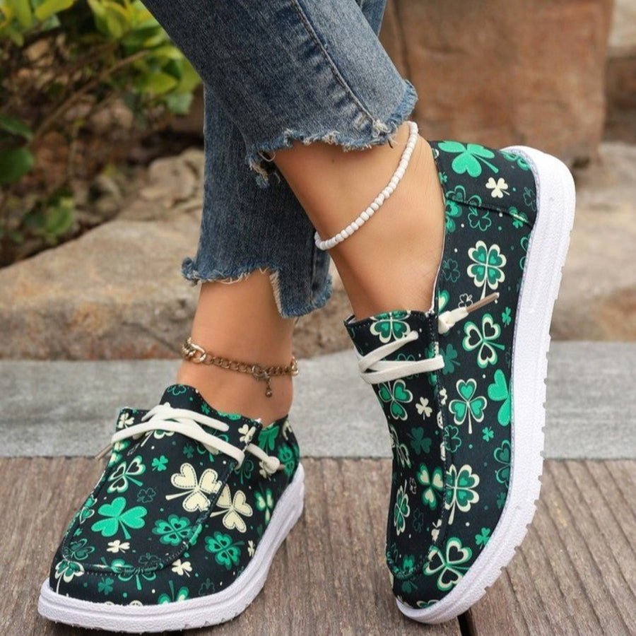 Clover print canvas slip-on sneakers with decorative white laces and white soles.
