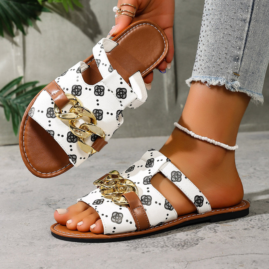 Patterned slide sandals in white with black graphic print and gold chain accent.
