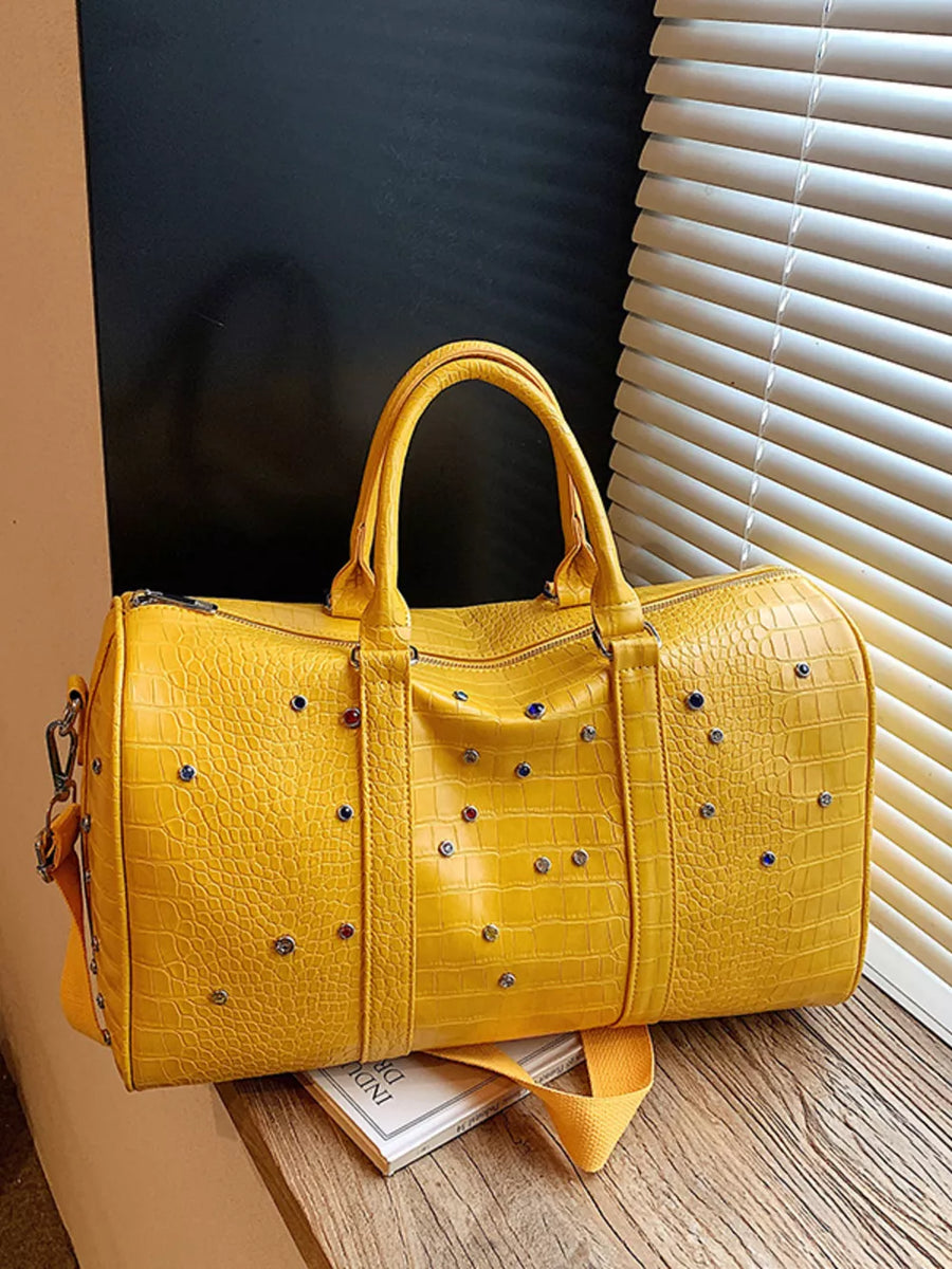 Yellow crocodile textured duffel bag with studded details and detachable strap.