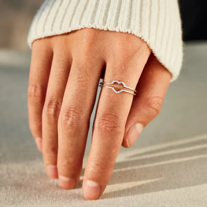 Silver double heart halo ring set with small stones on a hand wearing a white sweater