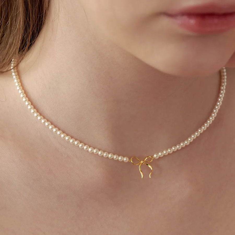 Delicate pearl choker necklace with a gold bow pendant.