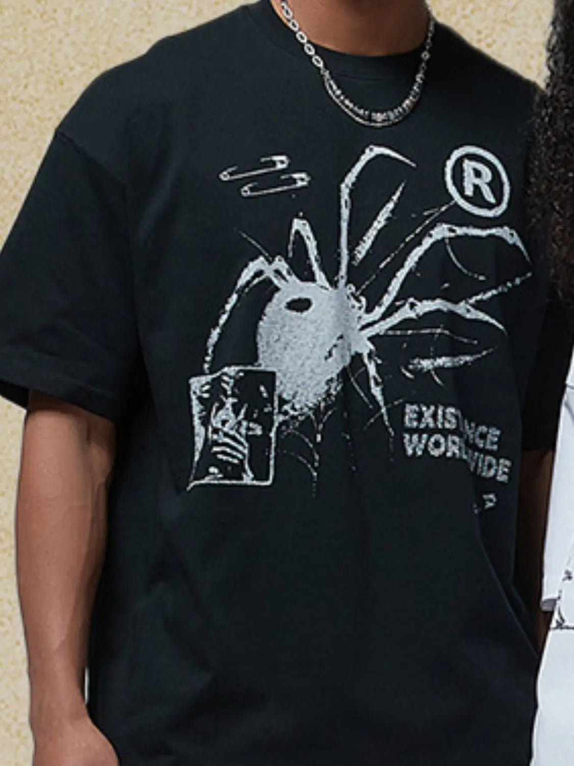 Black oversized graphic tee with spider print, safety pins, and text.