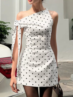 White polka dot mini dress with asymmetrical neckline and bow detail on sleeve.
