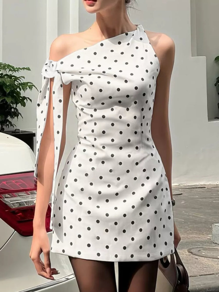 White polka dot mini dress with asymmetrical neckline and bow detail on sleeve.