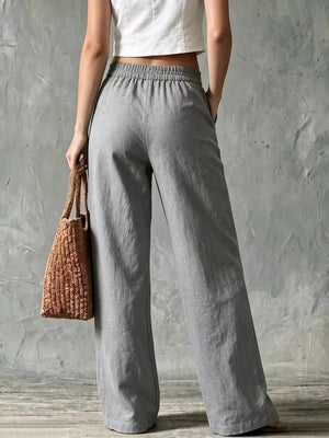 Wide leg linen pants in grey with elastic waistband and pockets, styled with a white crop top and straw bag.