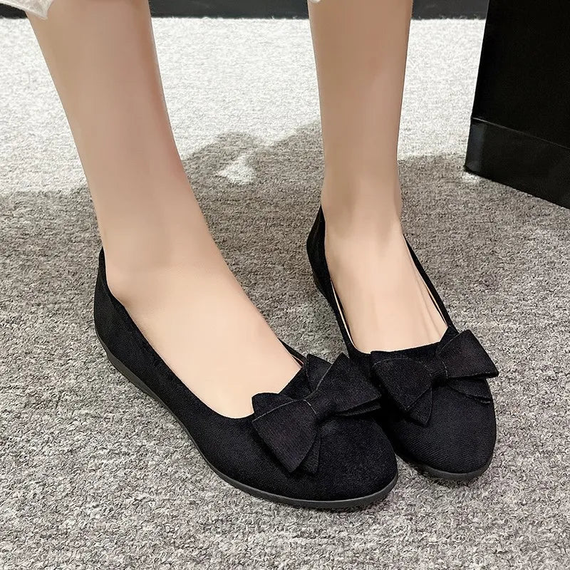 Black suede ballet flats with large bow embellishments.