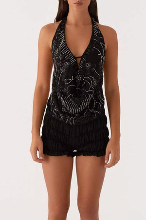 Black halter top with white embroidery and sequin detail, paired with ruched black shorts.