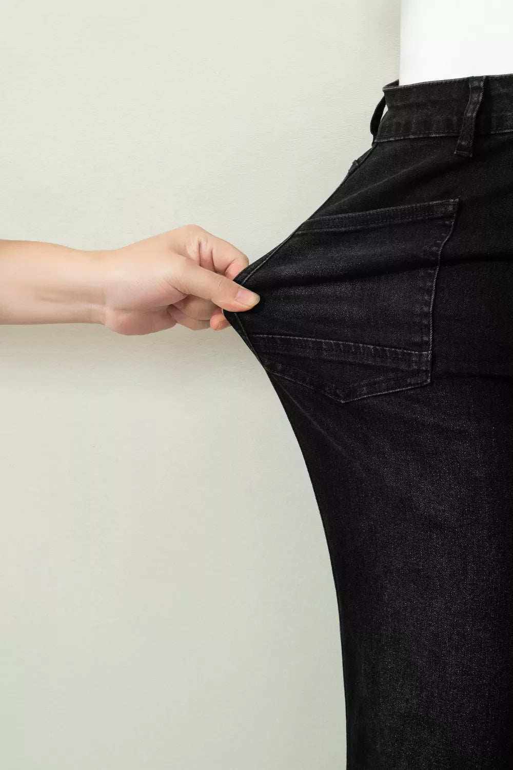 Black high-waisted cropped jeans with raw hem detail, showing stretch fabric.