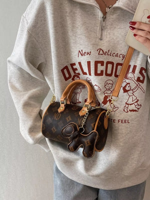 Mini barrel crossbody bag in brown monogram print with elephant charm and tan leather trim.