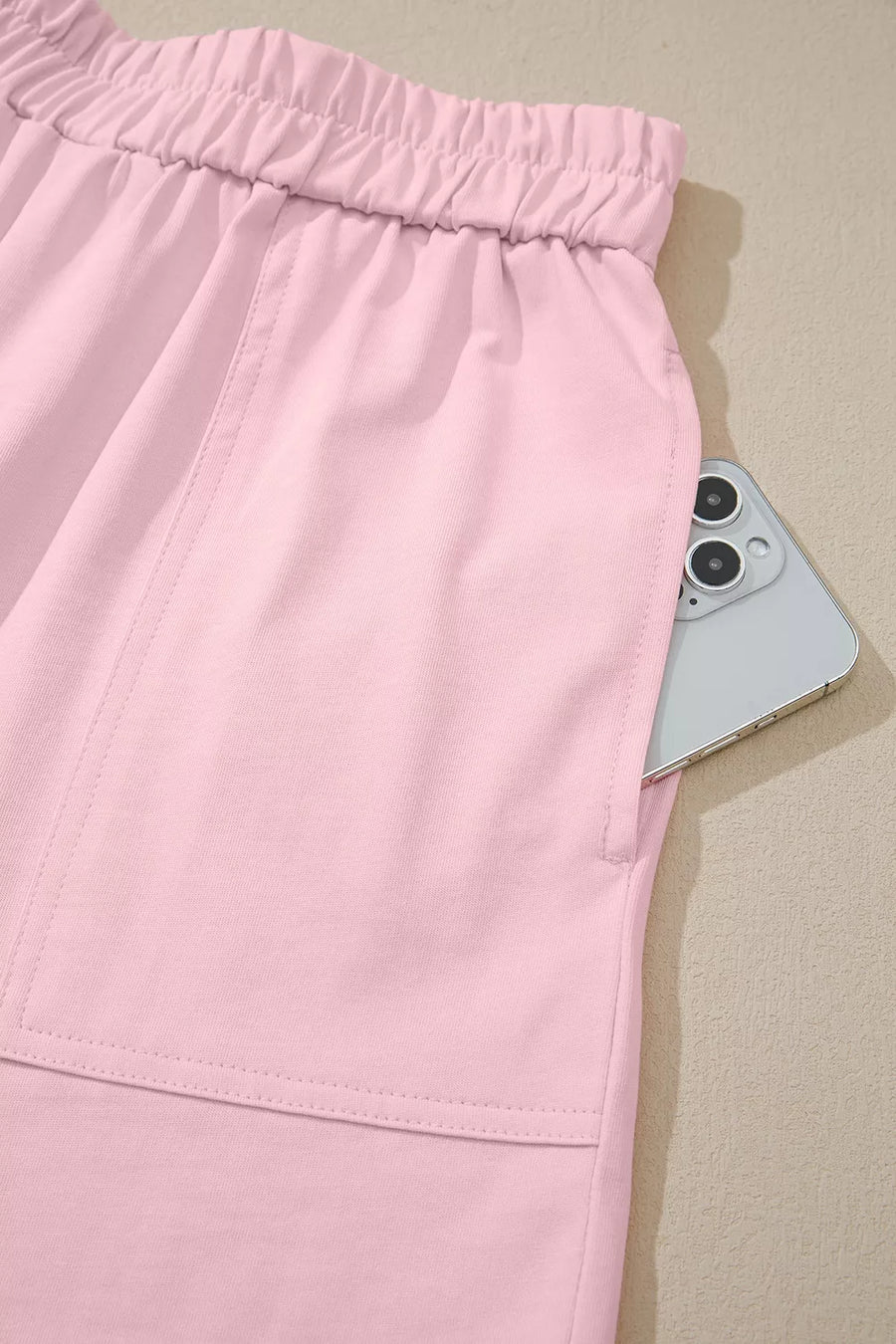 Blush pink pajama shorts with elastic waist and pocket holding a phone.
