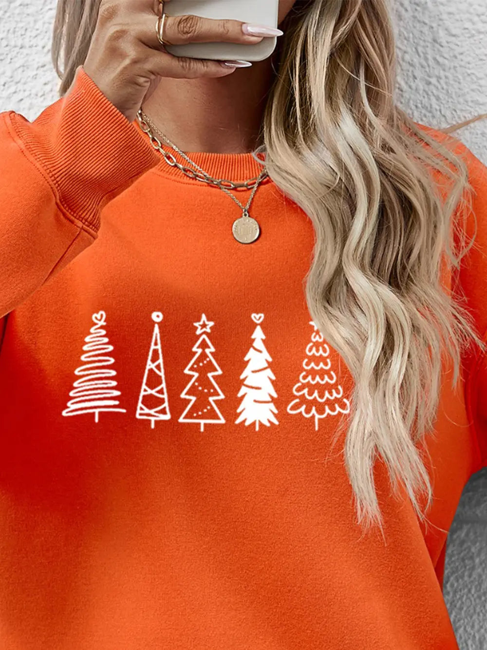 Orange crewneck sweatshirt with white festive tree line graphic.