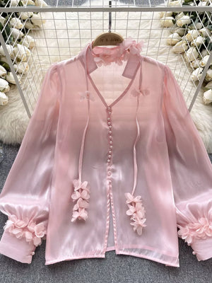 Pink sheer organza button-down shirt with floral appliqué details and bow ties.