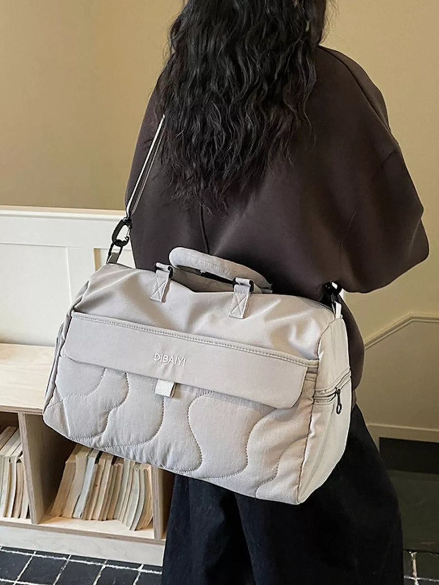 Light grey quilted duffel bag with adjustable strap and zippered side pocket.