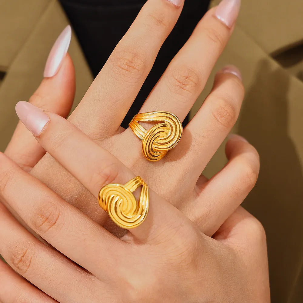 Gold ring with sculptural swirl design, 18K gold-plated, on a hand.