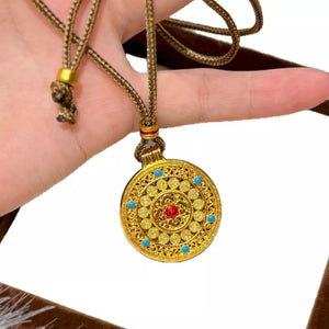 Gold-plated round pendant necklace with red and blue stones on a braided cord.