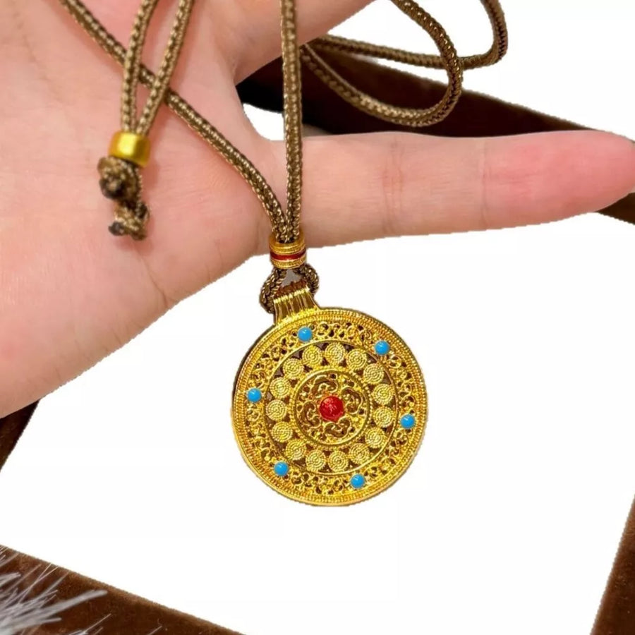 Gold-plated round pendant necklace with red and blue stones on a braided cord.