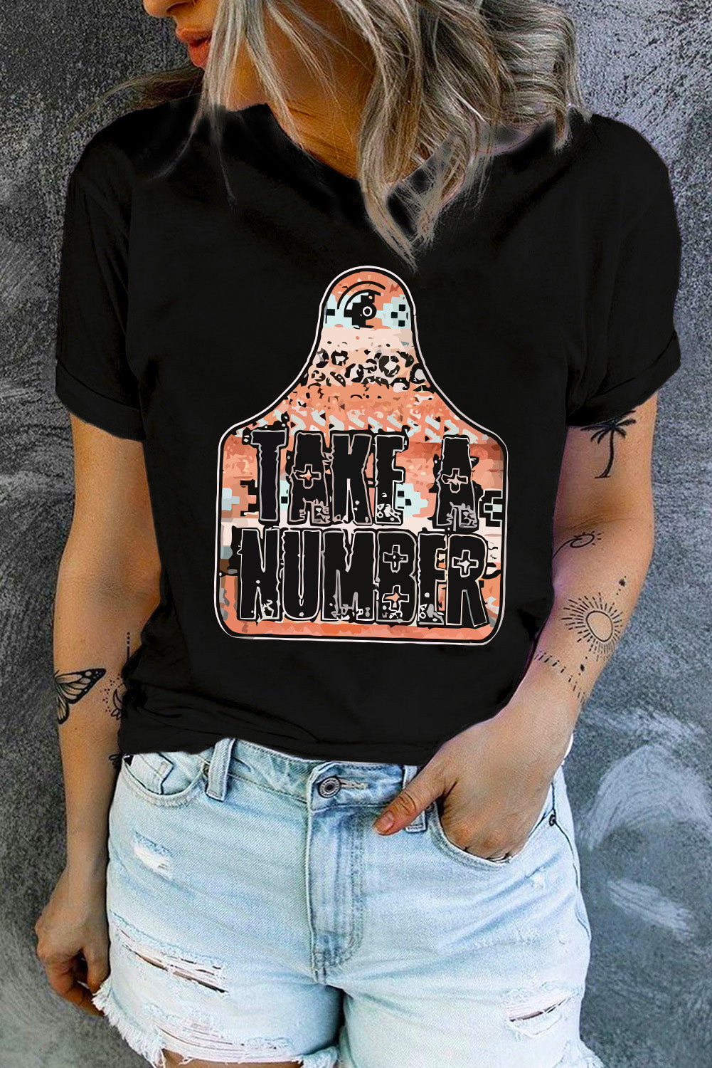 Black graphic t-shirt with Take A Number text on a tag shape with mixed patterns