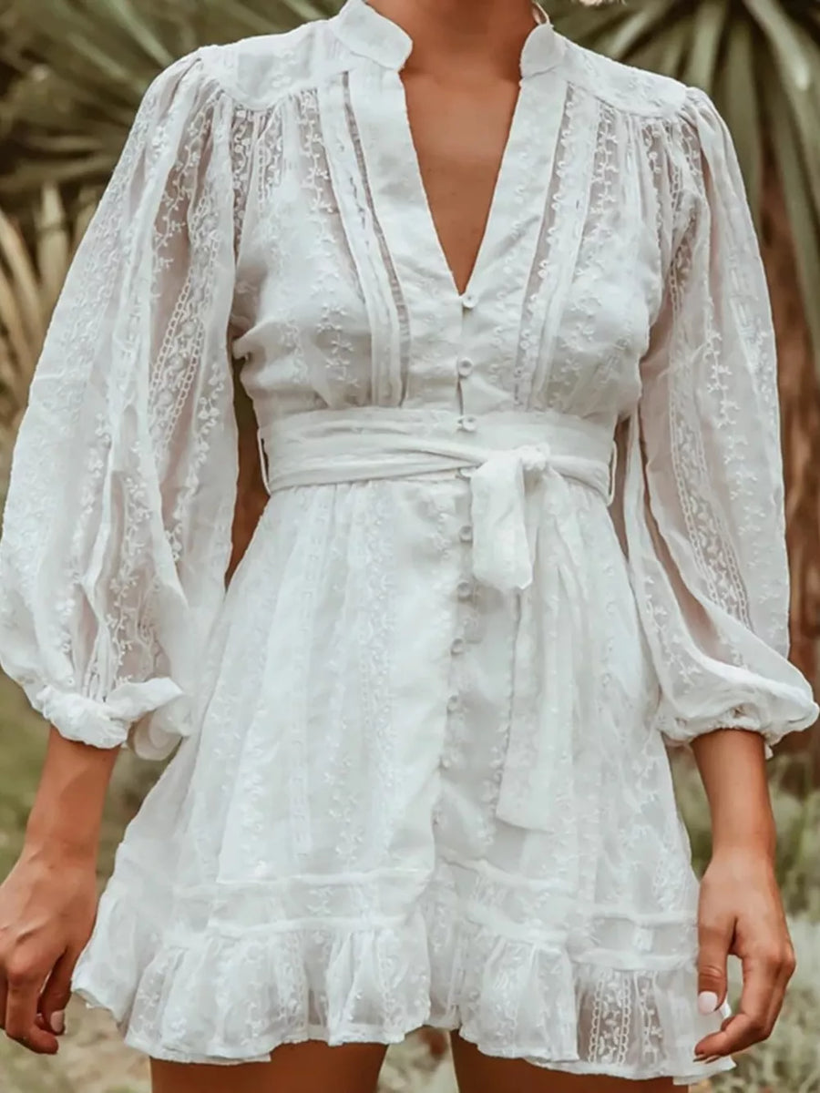 White lace mini dress with V-neck, bishop sleeves, and tie waist.