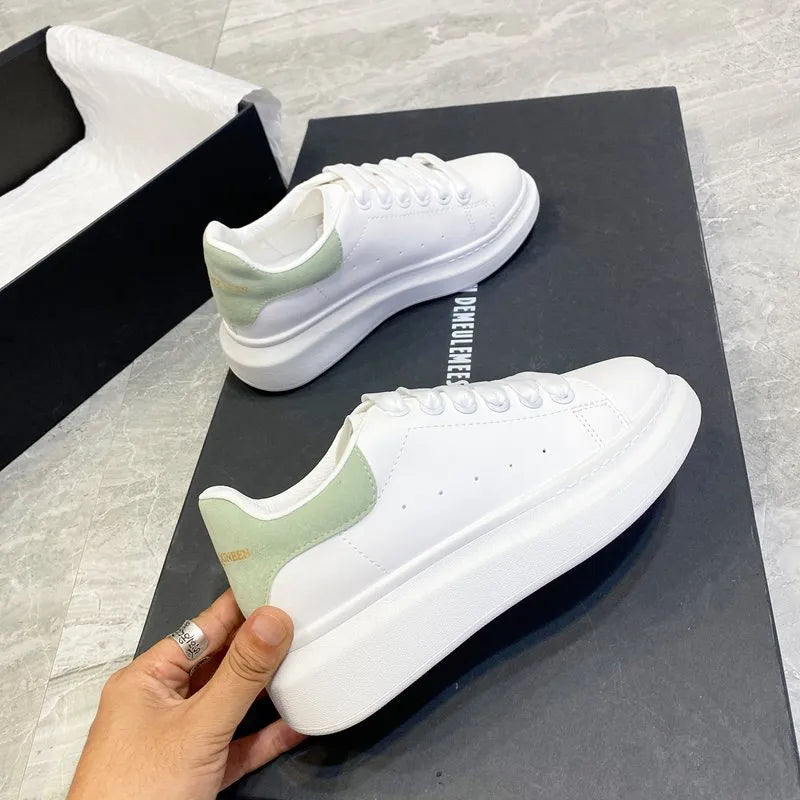 White platform sneakers with light green suede heel detail and white laces.