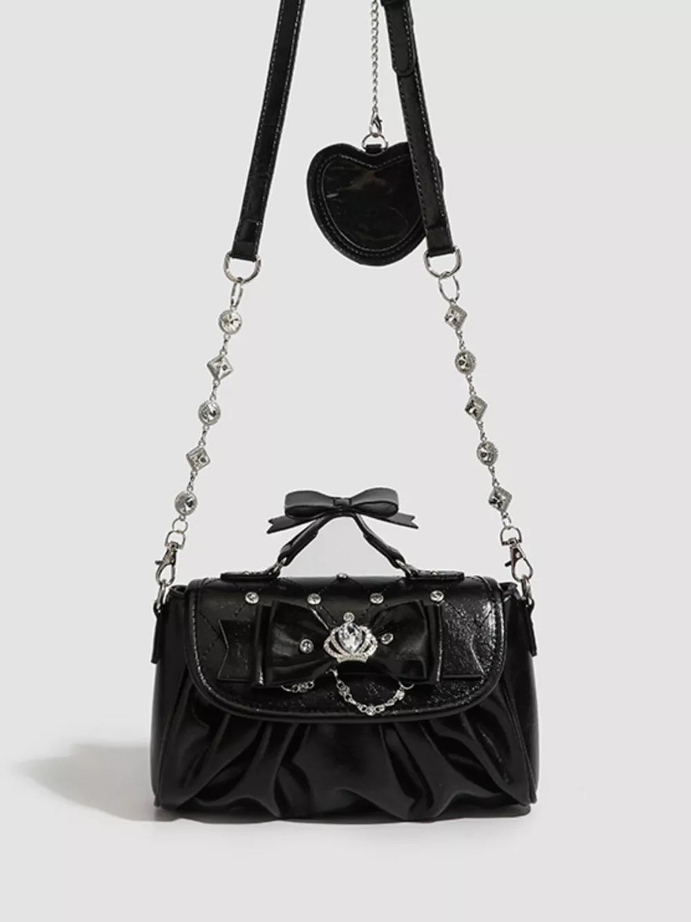 Black ruched crossbody bag with bow, crown detail, and heart charm.