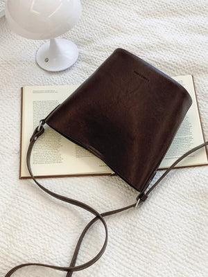Sleek leather bucket crossbody bag in chocolate brown with a long strap.