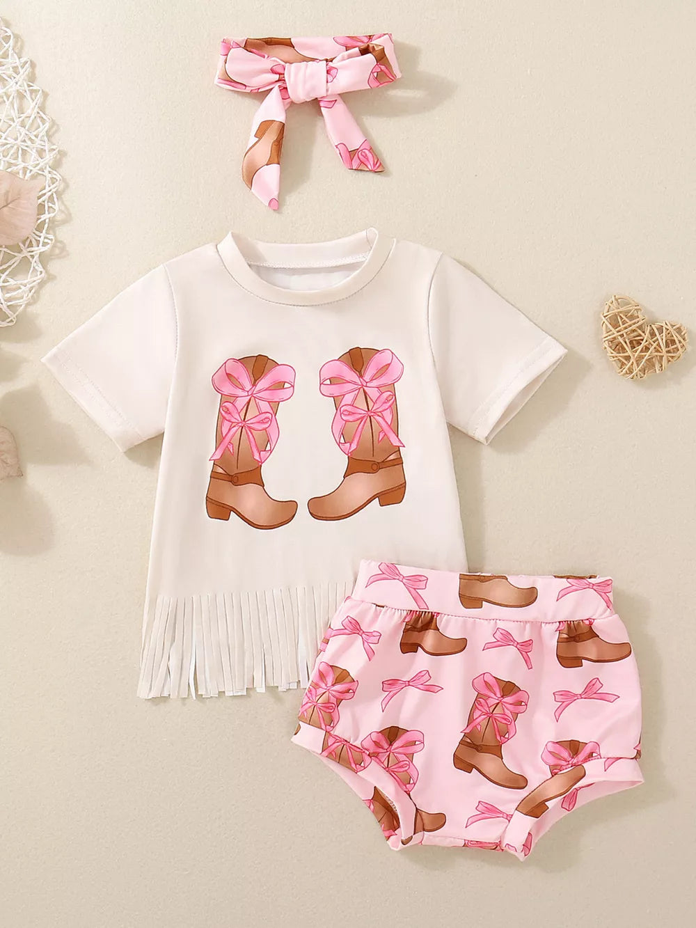 Baby outfit with white graphic tee featuring cowboy boots and fringe, pink printed shorts, and matching headband.