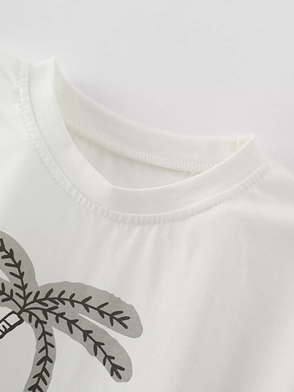 White cotton baby tee with playful abstract palm tree graphic and crew neck.