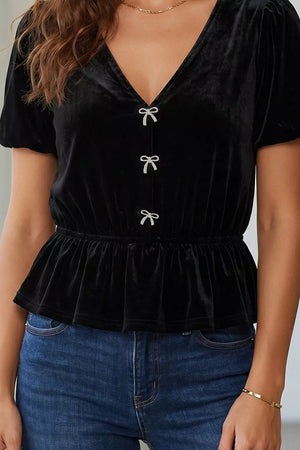Black velvet V-neck short sleeve peplum blouse with bow button details.