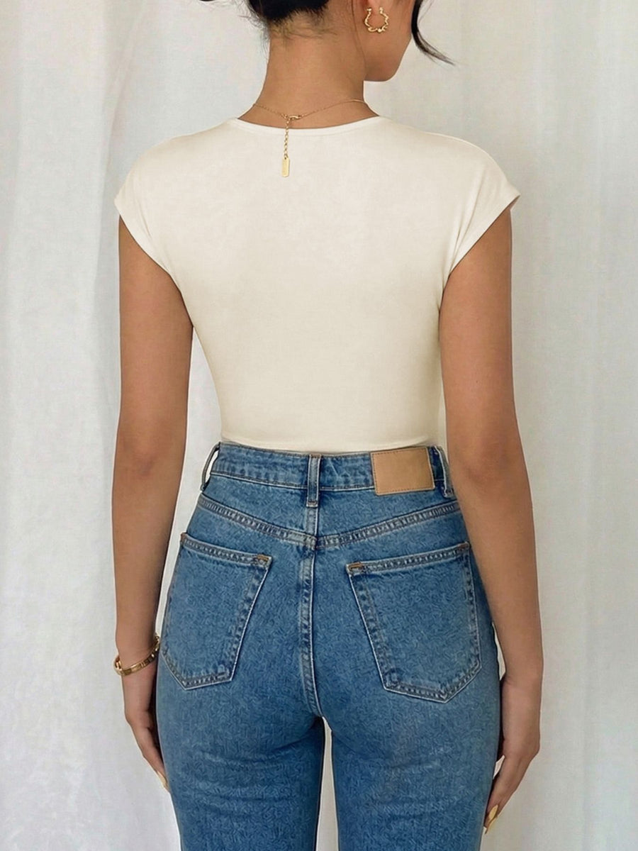 Cream cap sleeve bodysuit with surplice neckline, paired with high-waisted denim jeans.